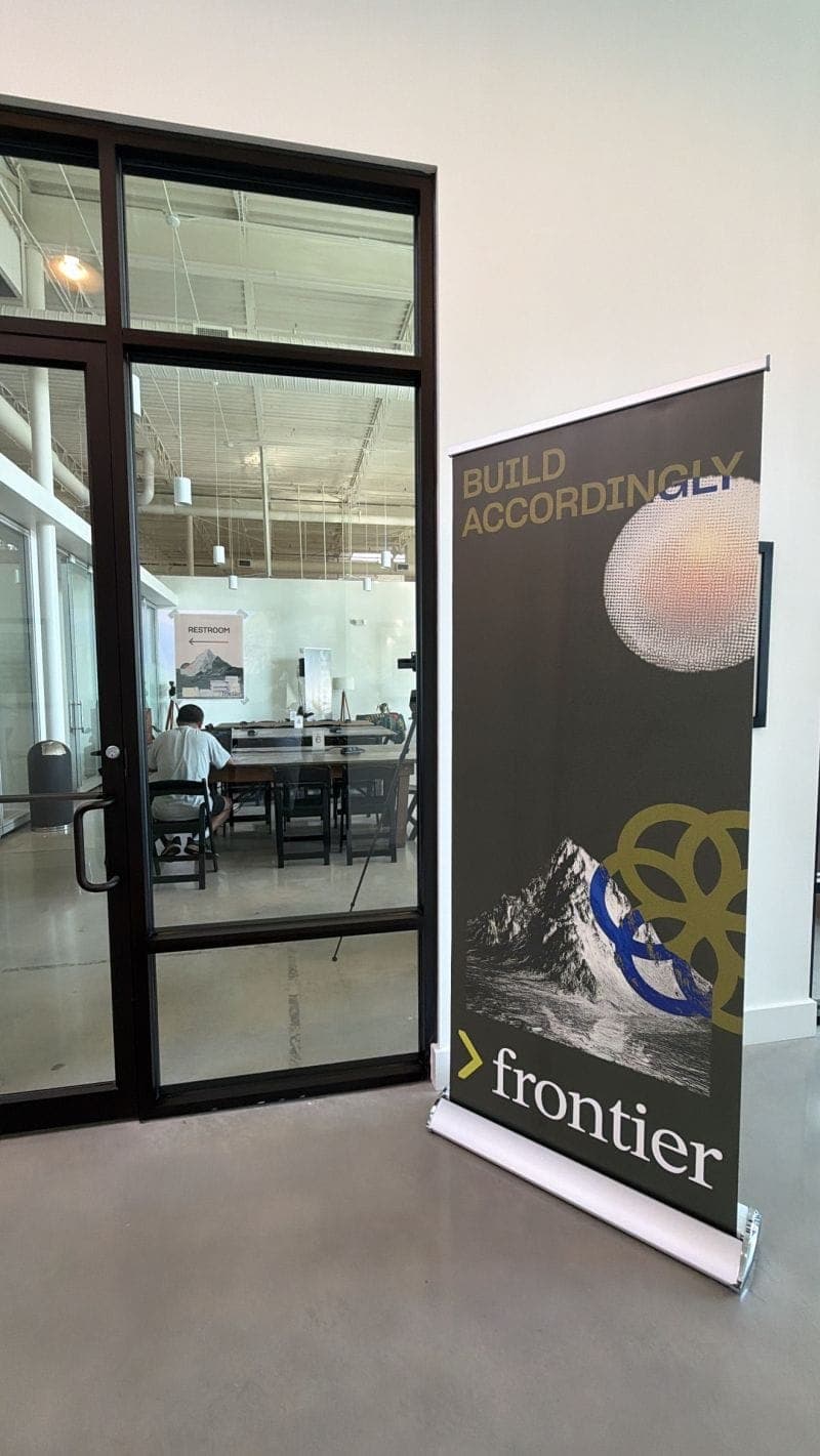 A Frontier banner reading Build Accordingly beside the glass doors of the build space.